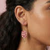 Close-up of a woman wearing pink floral earrings with gold accents.
