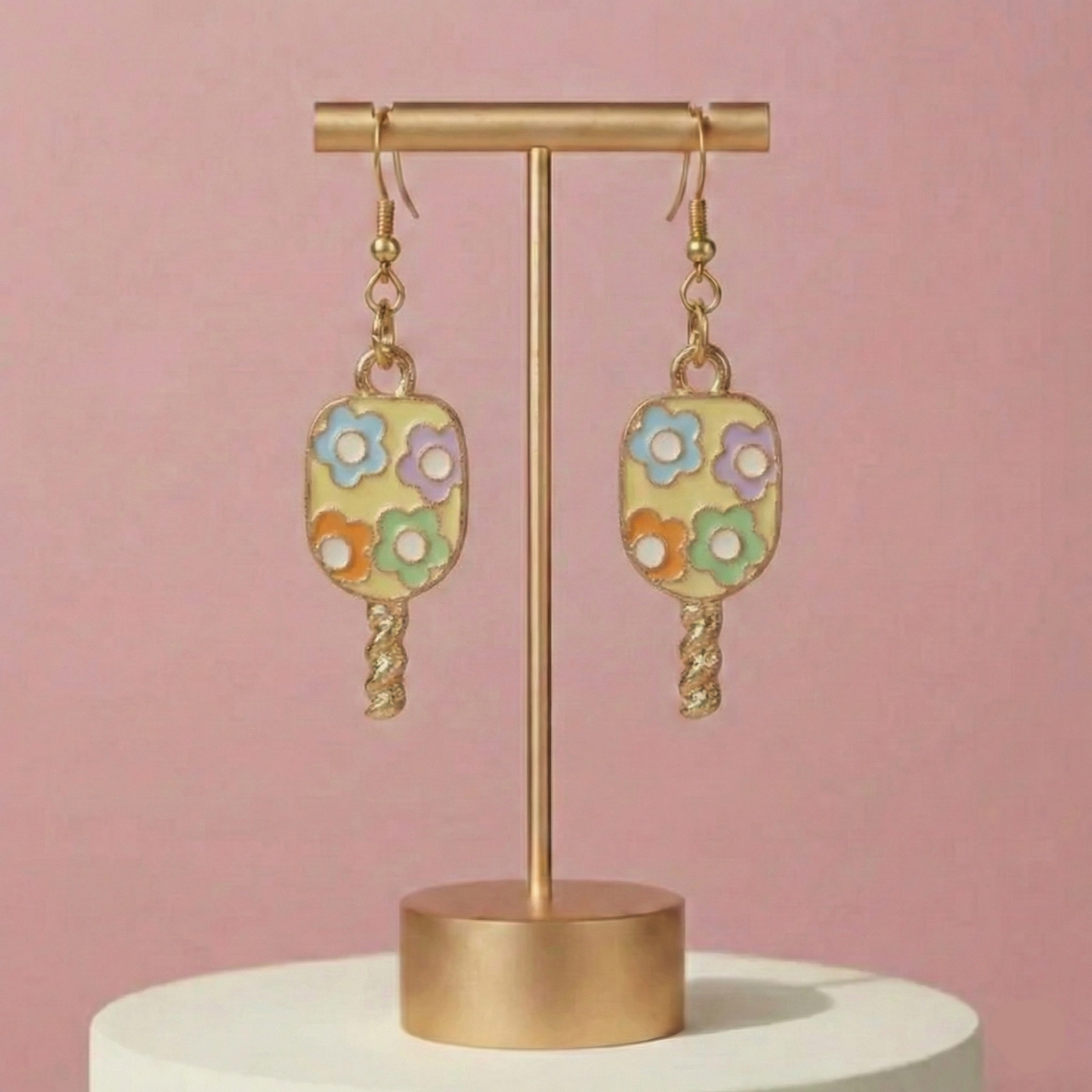 Floral earrings on a gold stand against a pink background