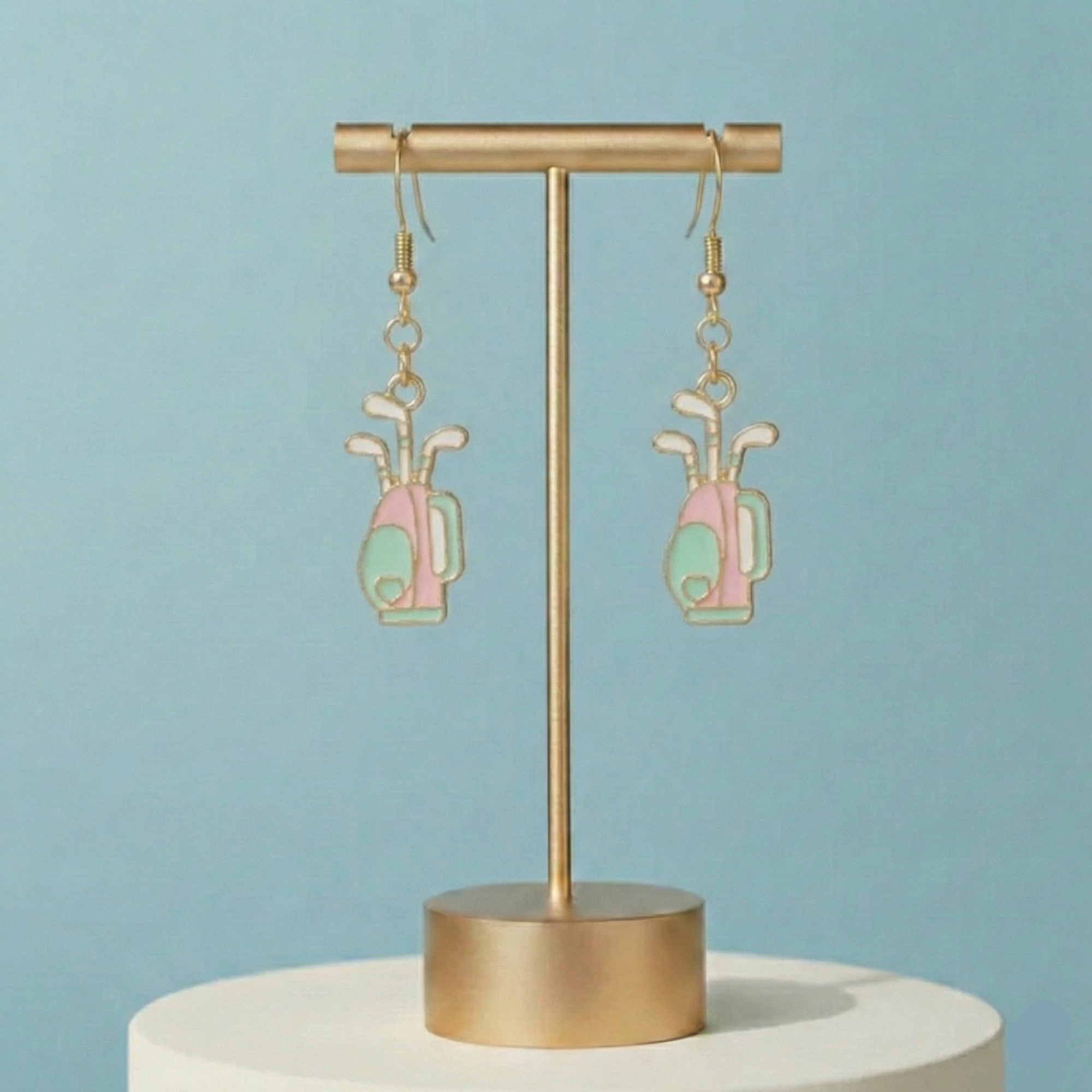 Gold earring stand with golf-themed earrings on a light blue background