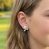 Close-up of a person wearing a floral earring outdoors with greenery in the background