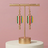 Colorful earrings on a gold earring stand against a pink background