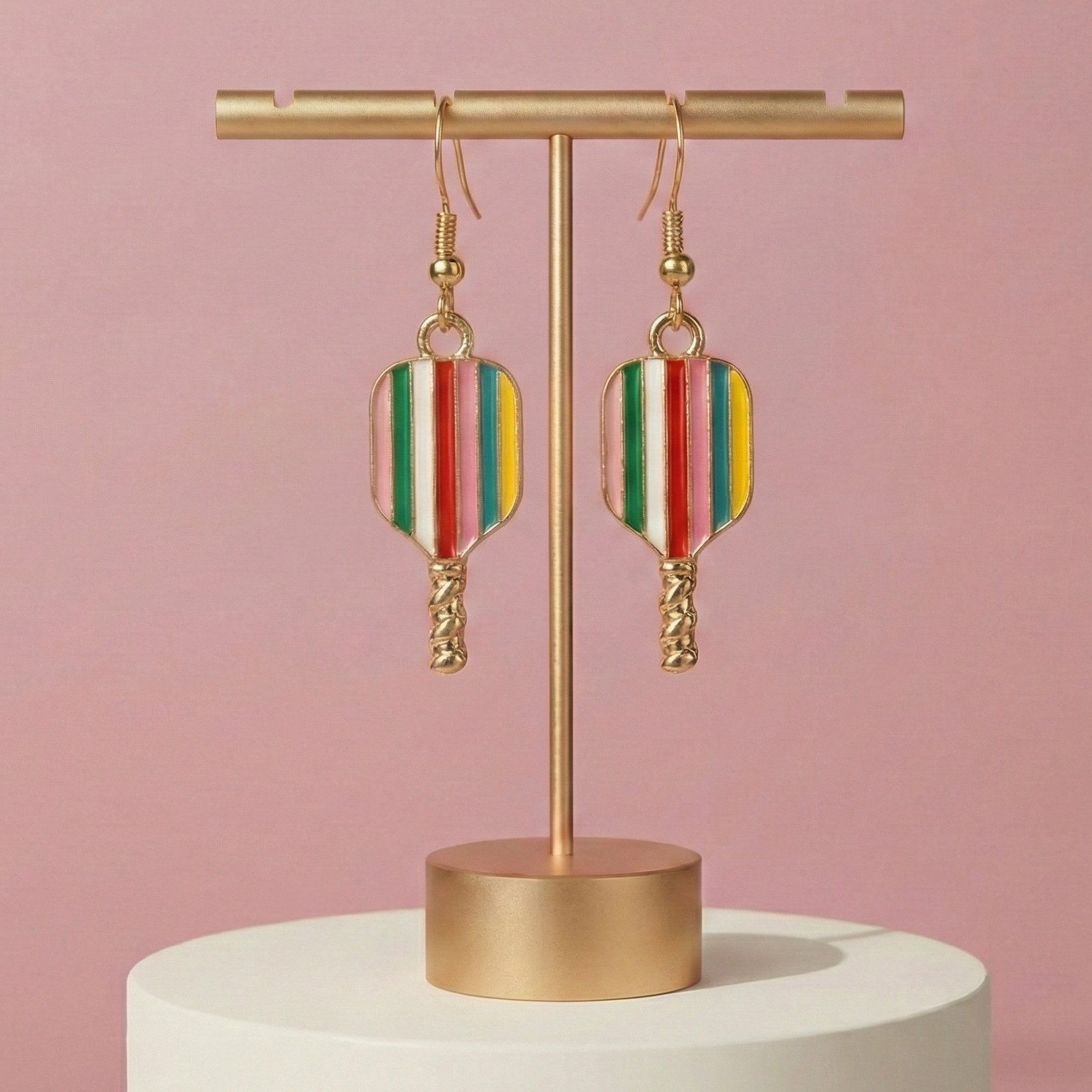 Colorful earrings on a gold earring stand against a pink background