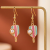 Pair of earrings with gold, pink, and turquoise design on a gold stand against a brown background