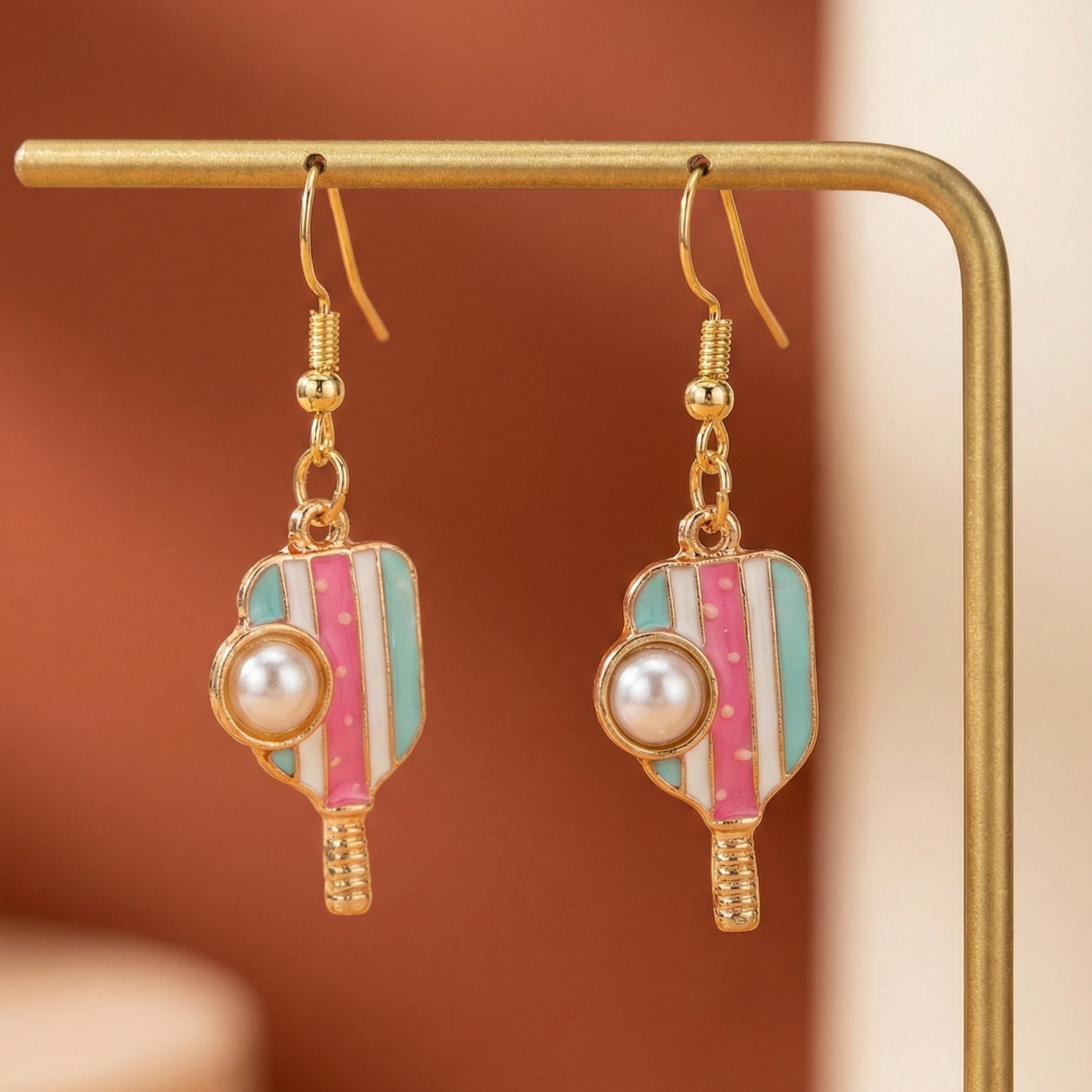 Pair of earrings with gold, pink, and turquoise design on a gold stand against a brown background